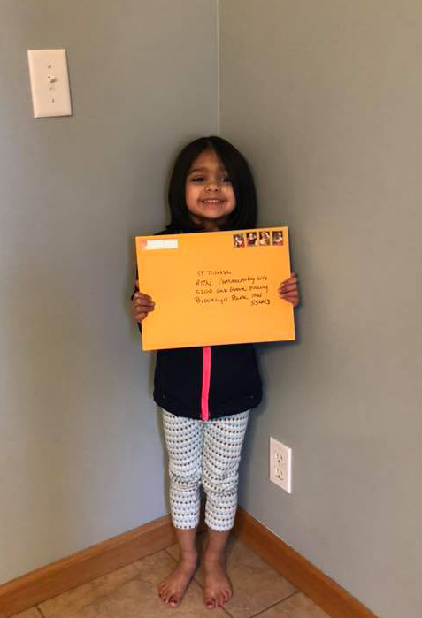 Little girl stands in living room holding large, yellow manila envelope addressed to Saint Therese at Oxbow Lake, Attention: Activities Team to boost residents' well-being. 